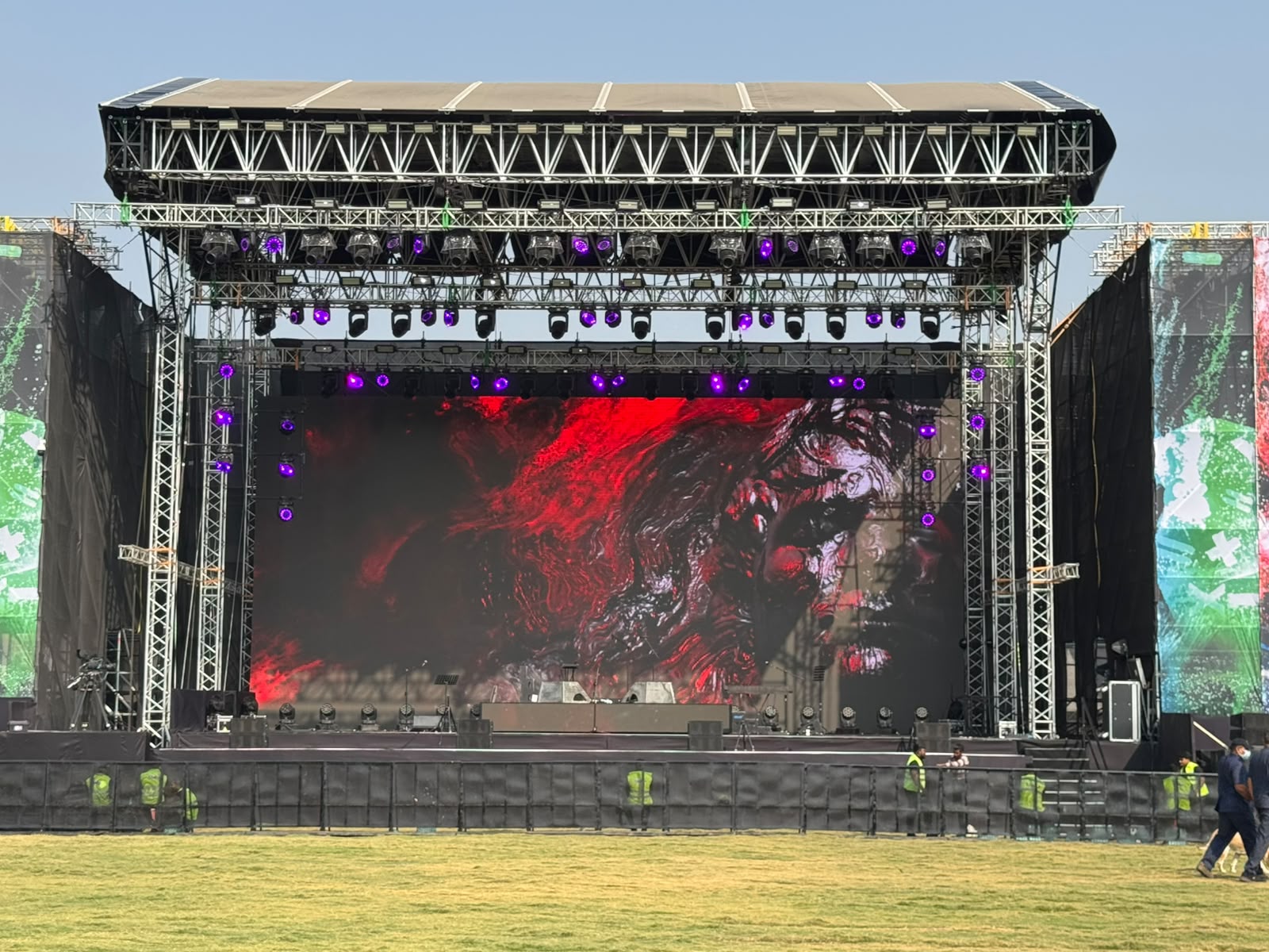 Outdoor festival main stage in daylight with wide red LED wall, moving heads and purple truss lighting