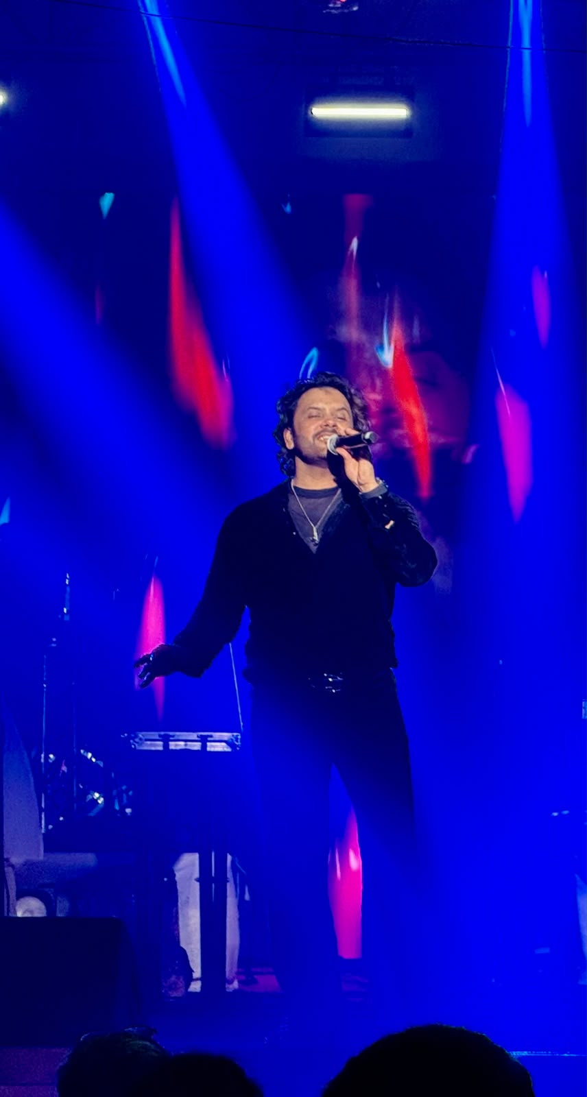 Male vocalist performing live under sweeping blue and red beam lights
