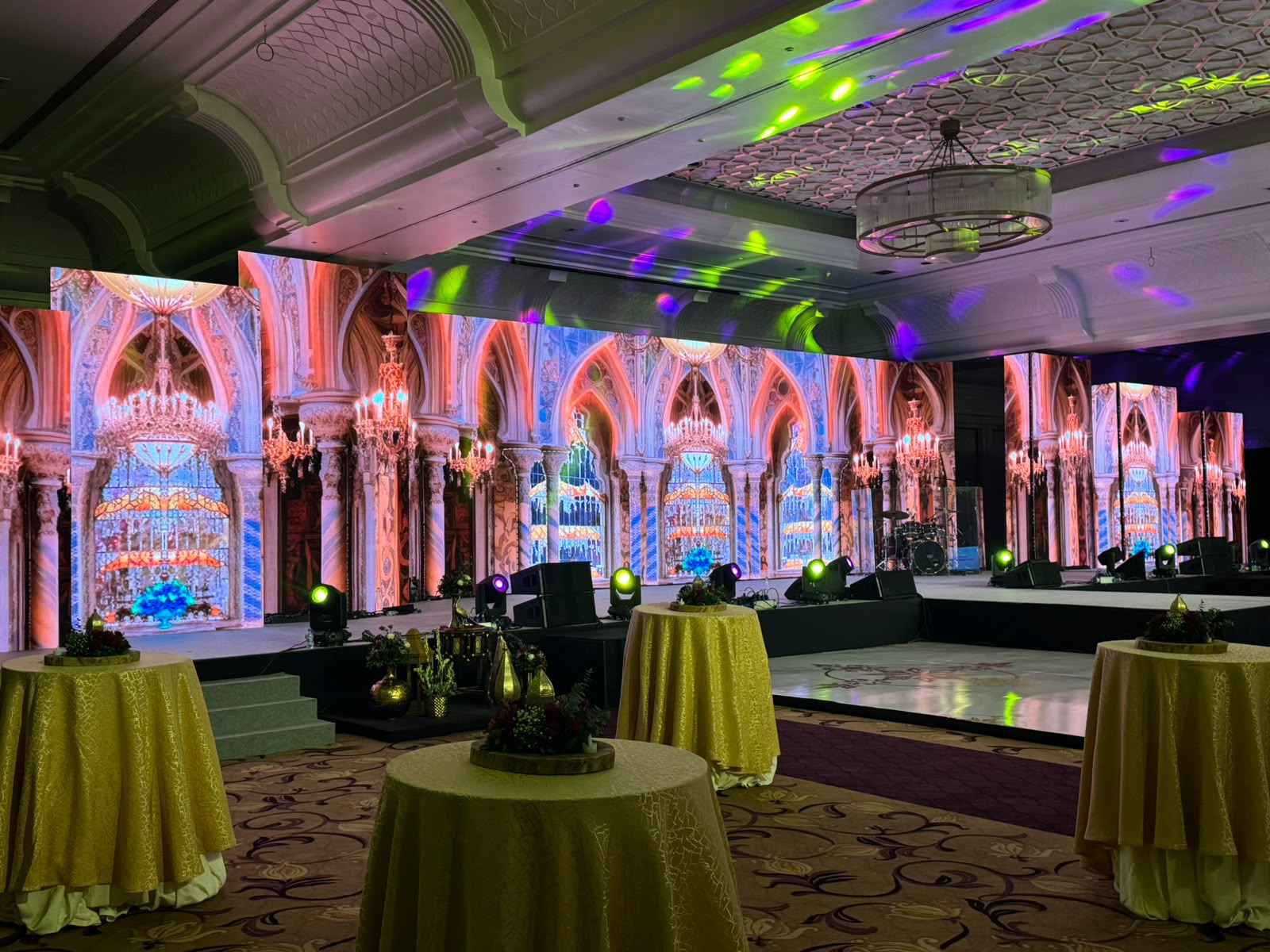 Luxury ballroom lounge with cathedral-style LED walls, gold linen tables and green and purple gobo lighting