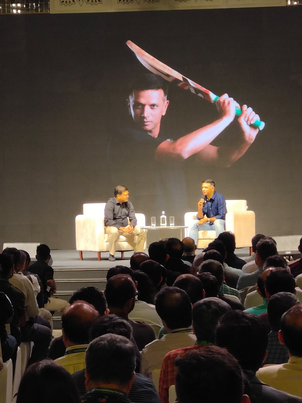 Rahul Dravid in conversation on stage with cricket bat visual on LED backdrop