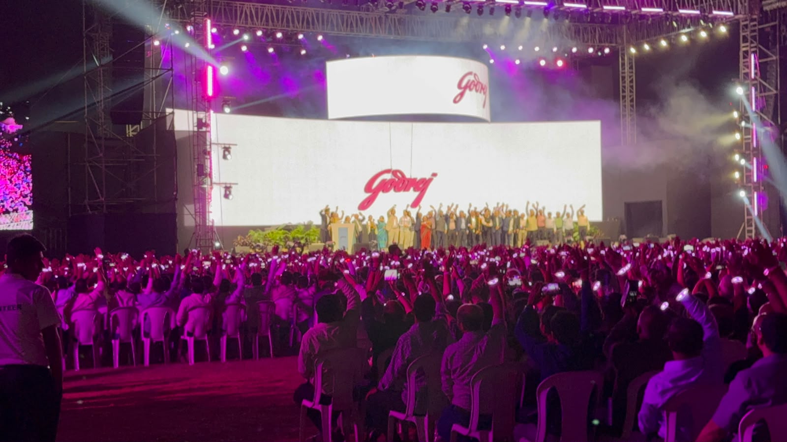 Godrej brand event with massive outdoor crowd holding phone lights, executives on stage and large LED wall