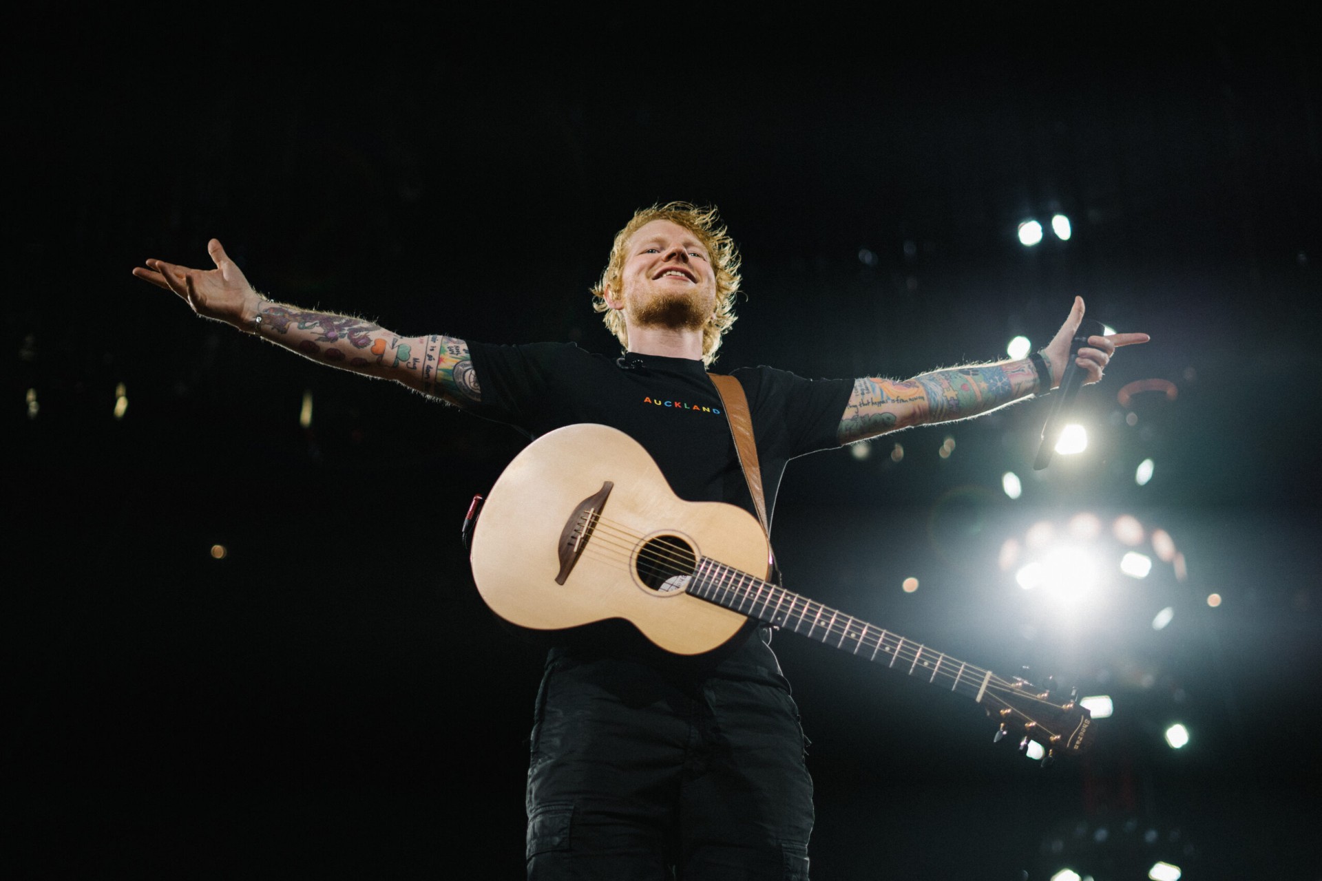 Ed Sheeran on stage with acoustic guitar and outstretched arms during his 2025 India Tour