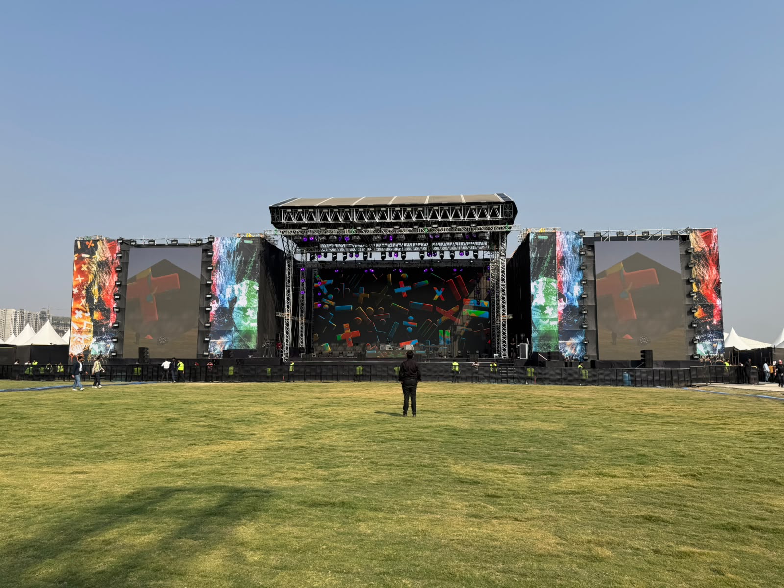 Outdoor daylight festival main stage with wide side LED walls, colorful geometric visuals and full truss roof