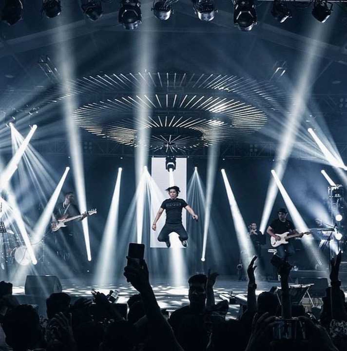 Performer mid-jump on arena stage with radial lighting rig